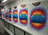 Coordinating hand-airbrushed name shirts displayed on studio easels, with blue graffiti lettering and colorful tie-dye bursts, showing matching group-order possibilities. Shirts sold individually.