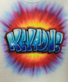 Keytons in blue dimensional graffiti lettering with black shadows and white highlights over a yellow, orange, red and purple tie-dye burst on a white shirt.
