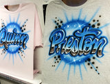 Quinn and Preston personalized shirts displayed on easels, showing blue chrome-effect block script with starbursts on pink and gray garments.