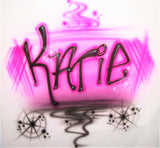 Original close-up of Katie hand-painted in black freestyle lettering with pink airbrush shading, sweeping black accents and stars on white fabric.