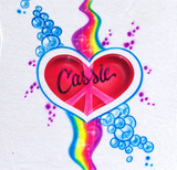 Cassie in black script across a pink-red peace heart, with a rainbow ribbon and blue bubbles on white fabric; digitally corrected shirt photograph.