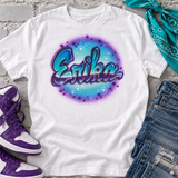 Styled mockup of a white Erika bubble-script airbrush shirt in turquoise, blue and purple, paired with purple high-top sneakers, denim and a teal bandana.