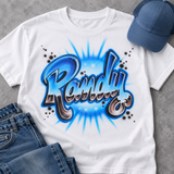 Styled mockup of a white T-shirt featuring the hand-airbrushed Randy name in blue chrome-effect block script, with swirls and starbursts.