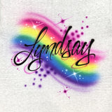 Original hand-painted Lyndsay name in flowing black script, with a soft rainbow background, purple bubbles and white star highlights on a white T-shirt.