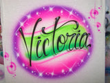 Original Victoria airbrush artwork in flowing black script over a green, pink and purple oval with bright starbursts on white fabric.