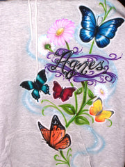 Several shaded butterflies and flowers form a tall composition down one side of the garment, finished with your name